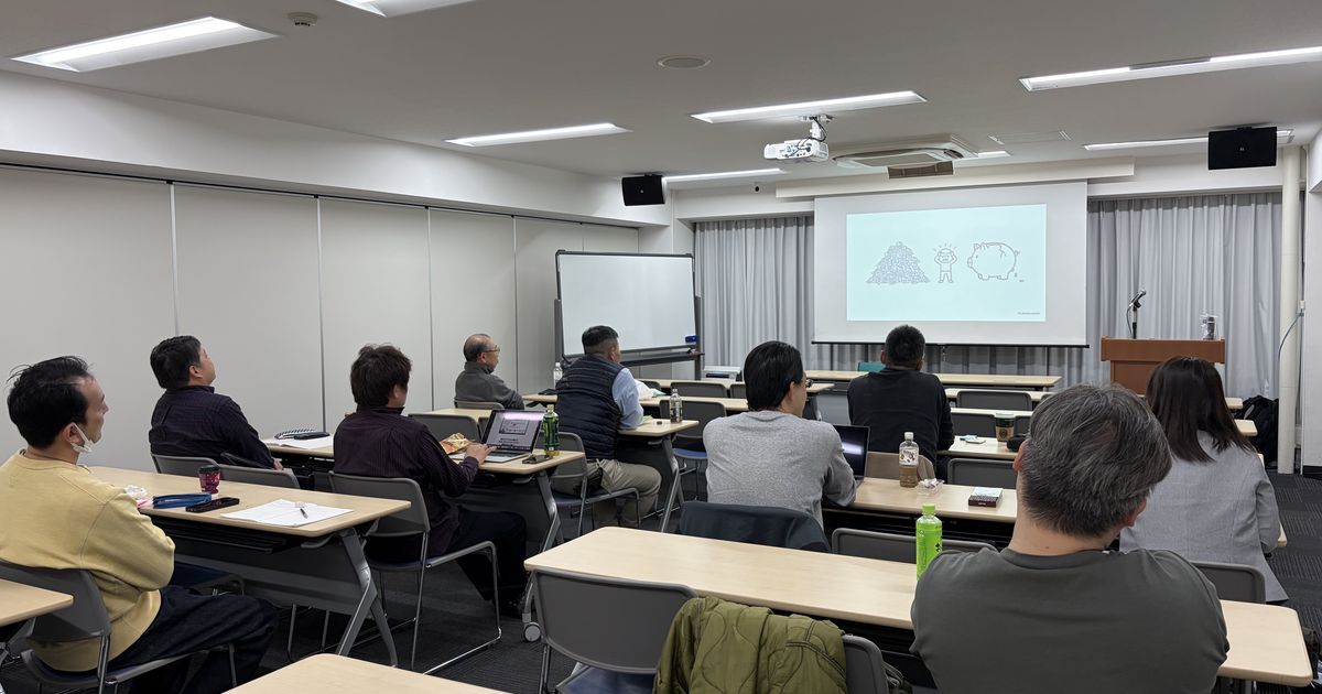 問題解決ワークの会場で、参加者がスクリーンの資料を見ながら話を聞いている様子