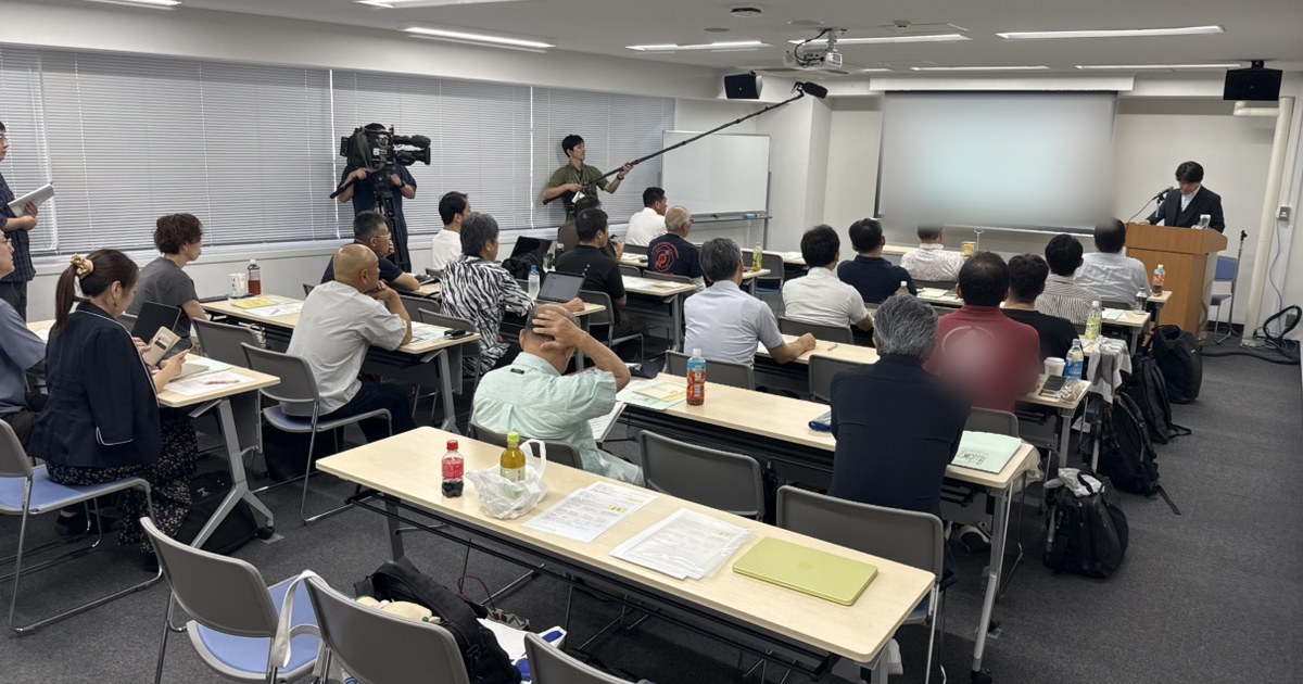 熊本地震チャリティーセミナーの会場。スクリーンの前で講演が行われ、畳店の参加者が机に向かい、取材のテレビカメラが撮影している